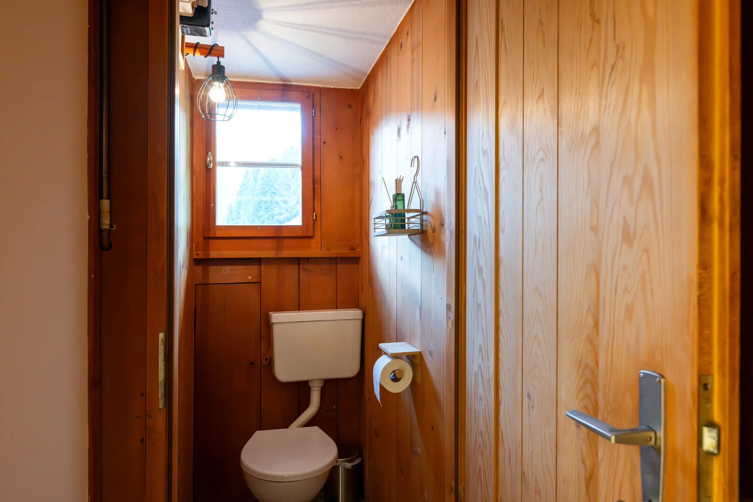 Das separate WC mit Holztäfer und kleinem Fenster, daneben die offene Tür mit Klinke.