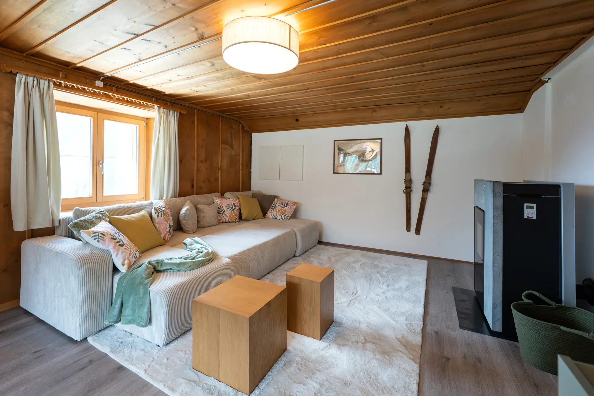 Wohnzimmer der Ferienwohnung 9° Ost mit Arvenholz an Wänden und Decke, Pelletofen und alten Skiern an der Wand